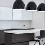Interior of modern kitchen with minimalist furniture and creative lamps hanging above counter and bar chairs